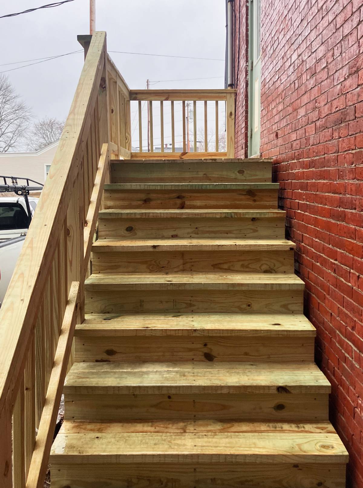 New wooden staircase and handrail beside a brick building, built by Henry